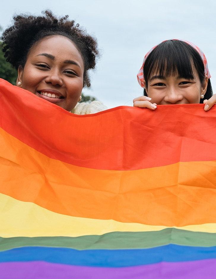 two students pose in back of a pride flag